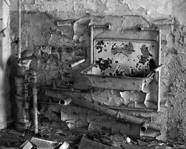 廃墟となった建物の中に錆びた洗面器とパイプの白黒写真 ロイヤリティフリーのストック画像