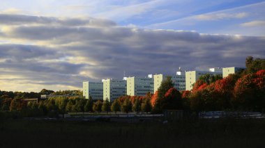 Stockholm 'deki üniversite binaları, bulutlu bir gökyüzünün altında sonbahar yapraklarıyla çevrili cam cephelerle çevrili..