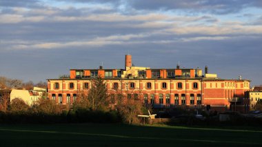 Çatısı terasları ve bacası akşam güneşiyle aydınlanan tarihi tuğla bina..