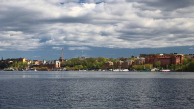Stockholm rıhtımının silueti dramatik bulutların altında sakin sularda baharda seyredildi.