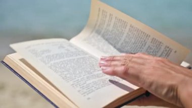 Sahil kenarındaki bir kadın kitap sayfalarını çeviriyor. Kapat. 