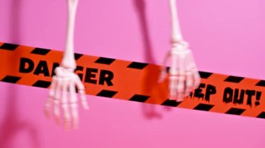 Lanetli Cadılar Bayramı Ambiansı: İskelet Eller pembe arka planda uyarı bantlarıyla
