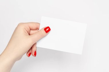 Close up, womans hands with red nails holding blank white paper sheet on a white background, copy space.