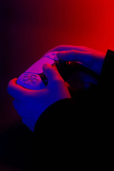 Modern white gamepad illuminated red and blue in male hands on a dark background, game controller for video games.