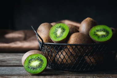 Still life with fresh kiwi fruit in a metal basket on a dark background, close-up.