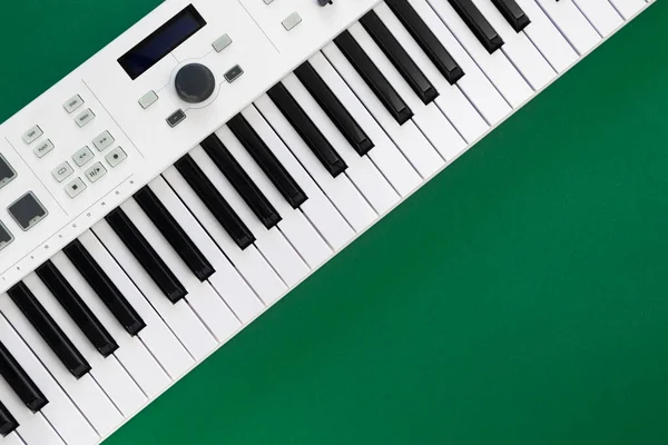 Midi keyboard on green background, flat lay, musical creativity concept, copy space.