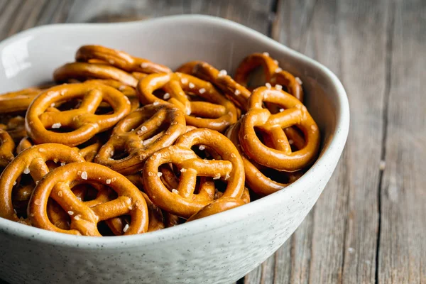 Mini pretzels with salt in a bowl on wooden background, close up.