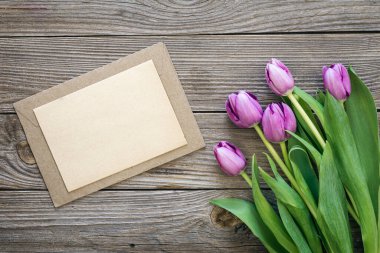 Bouquet of purple tulips and blank greeting card on wooden background, top view, copy space.