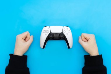 White gamepad and male hands on a blue background, the concept of winning, losing, flat lay.
