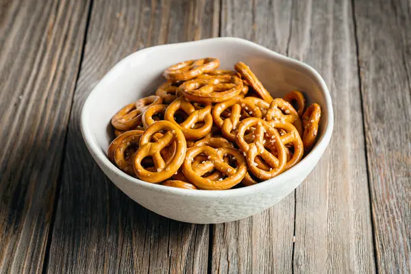 Mini pretzels with salt in a bowl on wooden background, close up.