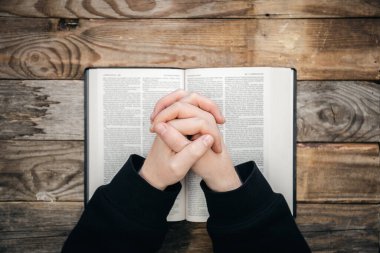 Yakın plan, Hıristiyan İncil okur. Elleri katlanmış kutsal bir İncil 'in üzerinde, ahşap arka planda, en üstte..