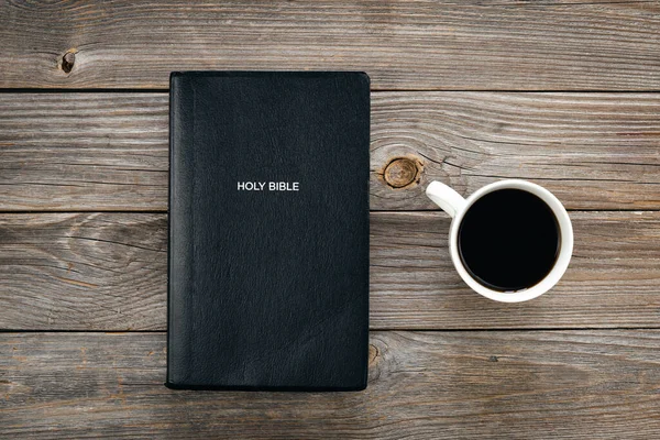 Black Bible and a cup of coffee on a wooden background, top view, concept of christian life, Bible study.