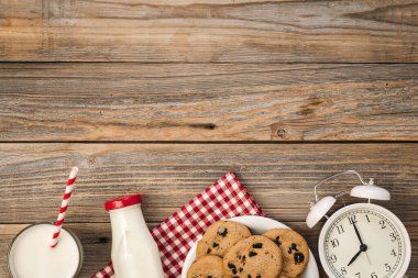 Süt, çikolata parçalı kurabiyeler ve ahşap zemin üzerinde beyaz alarm saati, üst görünüm, kopyalama alanı.