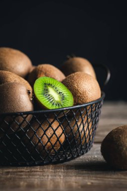 Still life with kiwi fruit in a metal basket on a wooden surface, close-up.