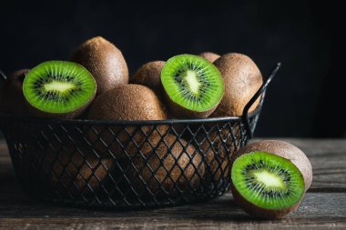 Still life with fresh kiwi fruit in a metal basket on a dark background, close-up.