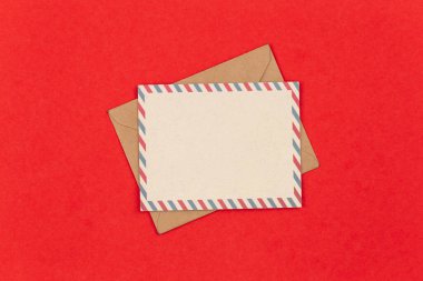 Posta zarfı ve boş kartpostal kırmızı arkaplan, düz uzanma, kopyalama alanı.
