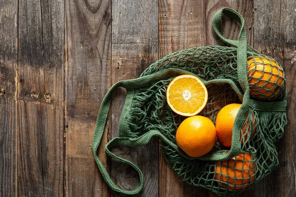 Fresh oranges in a string bag, eco-friendly product on a wooden background, copy space. No plastic, only natural materials and natural products.