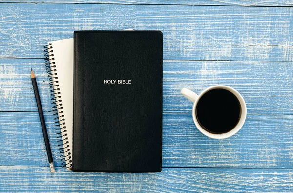 Holy Bible, notebook and coffee cup on blue wooden background, flat lay.