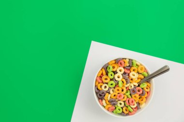 Colored breakfast cereal in a bowl on a green background, flat lay, childrens healthy breakfast, copy space.