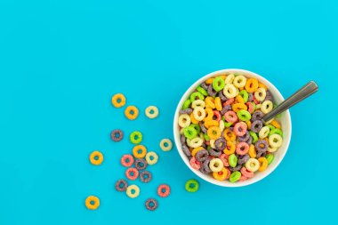 Colorful cereal in white bowl with spoon on a blue background, flat lay, copy space.