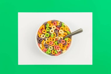 Colored breakfast cereal in a bowl on a green background, flat lay, childrens healthy breakfast, close up.
