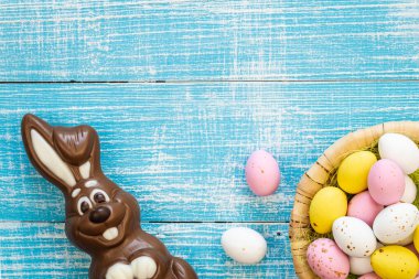Easter background with chocolate bunny and colorful chocolate eggs in a nest on a blue wooden background, flat lay, Easter holiday concept, childrens sweets, copy space.