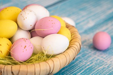 Easter candies, colorful chocolate eggs in a nest on a blue wooden background, the concept of the Easter holiday, a traditional dessert for children.