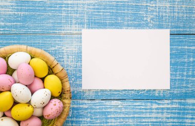 Easter background with colorful chocolate eggs and a blank piece of paper, on a blue wooden background, flat lay, Easter holiday concept, copy space.