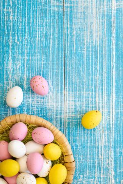 Easter candies, colorful chocolate eggs in a nest on a blue wooden background, top view, Easter holiday concept, traditional dessert for children, copy space.