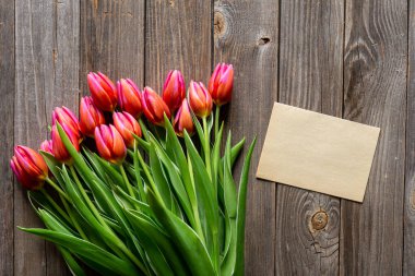 Bouquet of fresh pink tulips and a blank piece of paper on a wooden background, top view, concept of mothers day, womens day, spring background with a bouquet of flowers, rustic style, copy space.