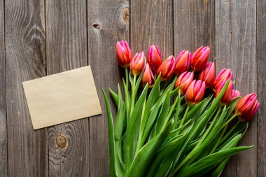 Bouquet of fresh pink tulips and a blank piece of paper on a wooden background, top view, concept of mothers day, womens day, spring background with a bouquet of flowers, rustic style, copy space.