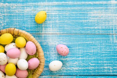 Easter candies, colorful chocolate eggs in a nest on a blue wooden background, top view, Easter holiday concept, traditional dessert for children, copy space.