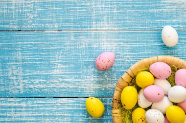 Easter candies, colorful chocolate eggs in a nest on a blue wooden background, top view, Easter holiday concept, traditional dessert for children, copy space.