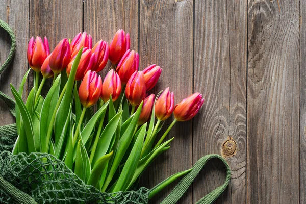 Bouquet of fresh pink tulips in a string bag on a wooden background, top view, concept of mothers day, womens day, spring background with a bouquet of flowers, rustic style.