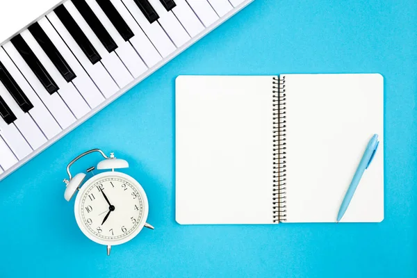 青い背景のブランクノートブック ピアノとホワイト目覚まし時計 トップビュー 音楽レッスンの概念 創造性と創造性 コピースペース — ストック写真