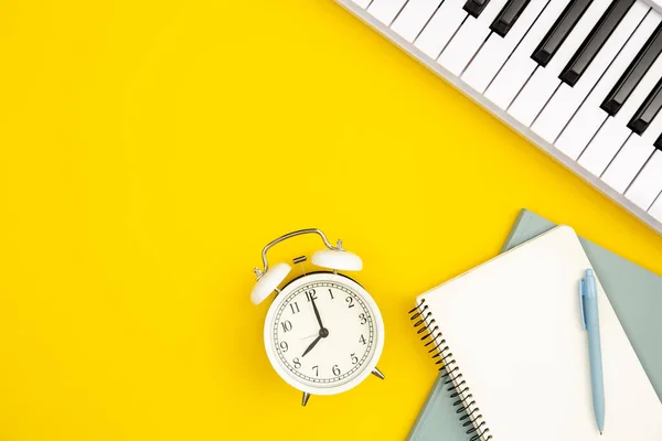 黄色の背景に白い目覚まし時計 ノートとピアノ トップビュー 音楽教育と創造性 白いシンセサイザー フラットレイアウトの概念 — ストック写真