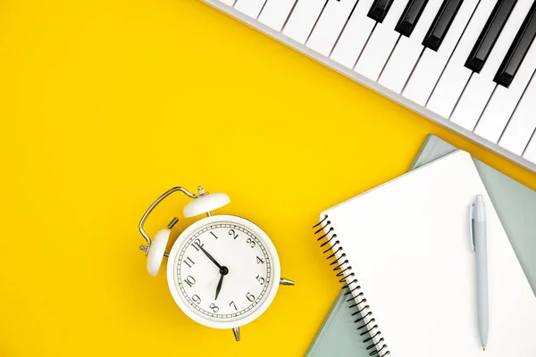 White alarm clock, notebooks and piano on a yellow background, top view, the concept of music education and creativity, white synthesizer, flat lay.