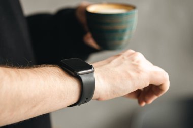 Elinde kahve fincanı olan adam çalışma saatinde akıllı saatini kontrol ediyor, iş ve teknoloji konsepti, kapatın, boşluğu kopyalayın..