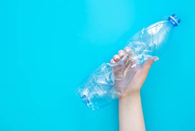 Mavi arka planda bir kadının elindeki plastik şişe kullanılmış. Üst manzara, düz yatak. Plastik kullanma kavramı. Çevresel sorun, küresel çevre sorunu, kopyalama alanı.