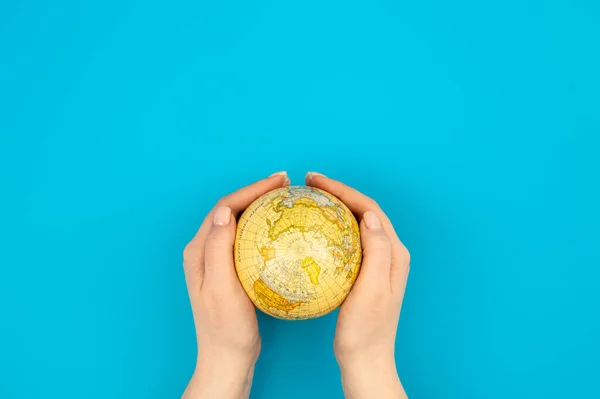 Earth globe in female hands on a blue background isolated, top view, Earth Day concept, care for the planet.