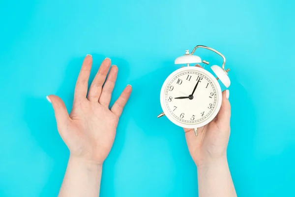 stock image White alarm clock in female hands on a blue background, top view, concept of time management, deadline and work in the office.