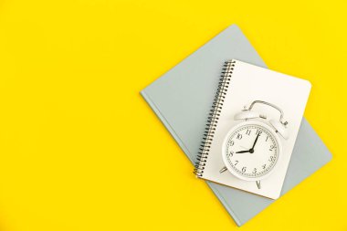 Beyaz alarm saati ve sarı arkaplanda boş not defteri, düz konum, kopyalama alanı.