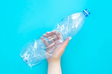 Mavi arka planda bir kadının elindeki plastik şişe kullanılmış. Üst manzara, düz yatak. Plastik kullanma kavramı. Çevresel sorun, küresel çevre sorunu, kopyalama alanı.