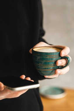 Akıllı telefon ve el yapımı seramik kahve yakın plan bir adamın elinde, teknolojiyi kullanma kavramı, ofiste sabah.