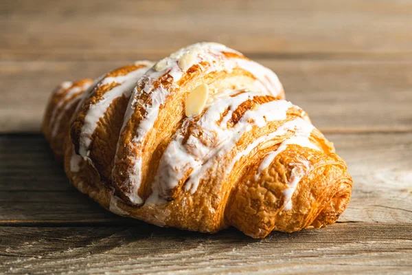 Freshly baked appetizing almond croissant covered with glaze, close-up on a wooden background, macro shot.