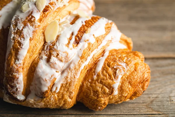 Freshly baked appetizing almond croissant covered with glaze, close-up on a wooden background, macro shot.