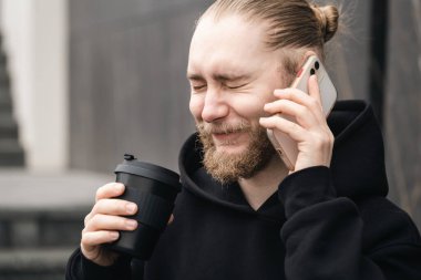 Ciddi bir genç sakallı akıllı telefon kullanır ve kahve içer. Yeniden kullanılabilir çevre dostu sürdürülebilir elverişli bambu kabı sıfır atık, plastik kavram yok.