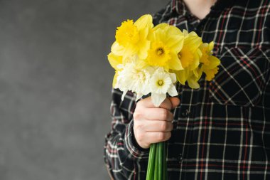 Bulanık gri arkaplanda özel bir tarih için nergis buketi tutan bir adam, boşluğu kopyala.