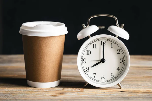 stock image Cardboard Coffee Aroma, Disposable Craft Cup and white Alarm Clock on Rustic Background. Office concept.