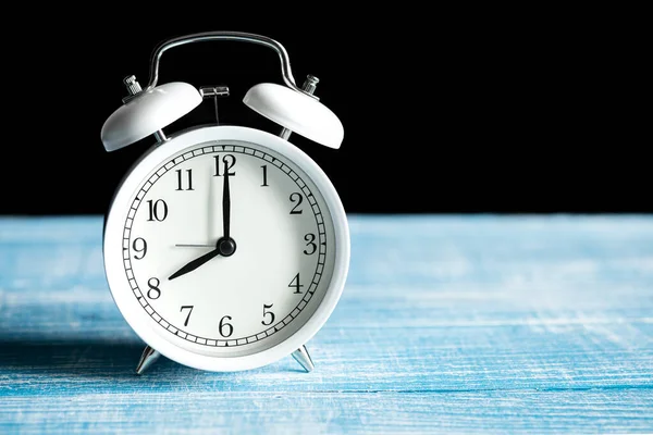 stock image Close-up, white Alarm clock shows 8 am on a blurred dark background, the concept of Morning at work, breakfast time, deadline, Copy space.